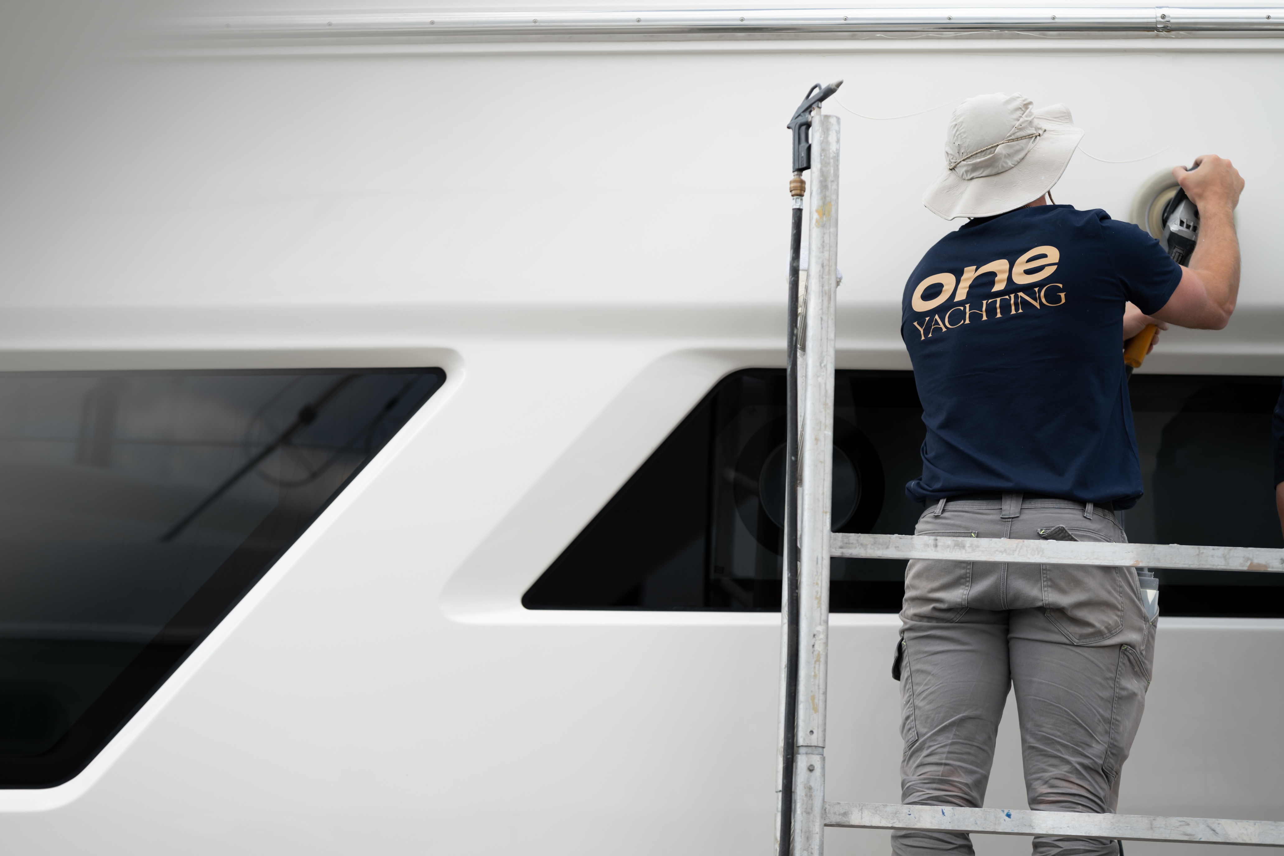 A man standing on a ladder painting the side of a boat.
